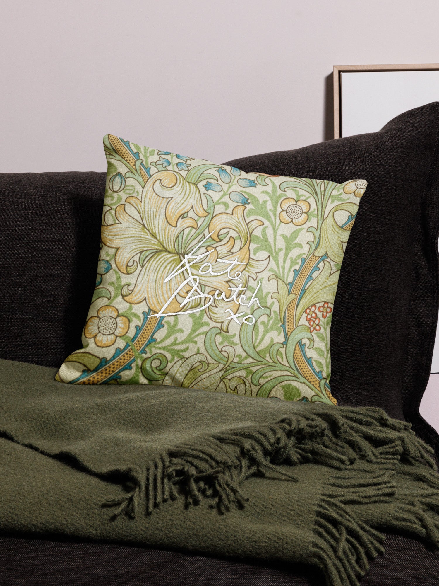 Decorative pillow with floral pattern and text on a couch with a green blanket