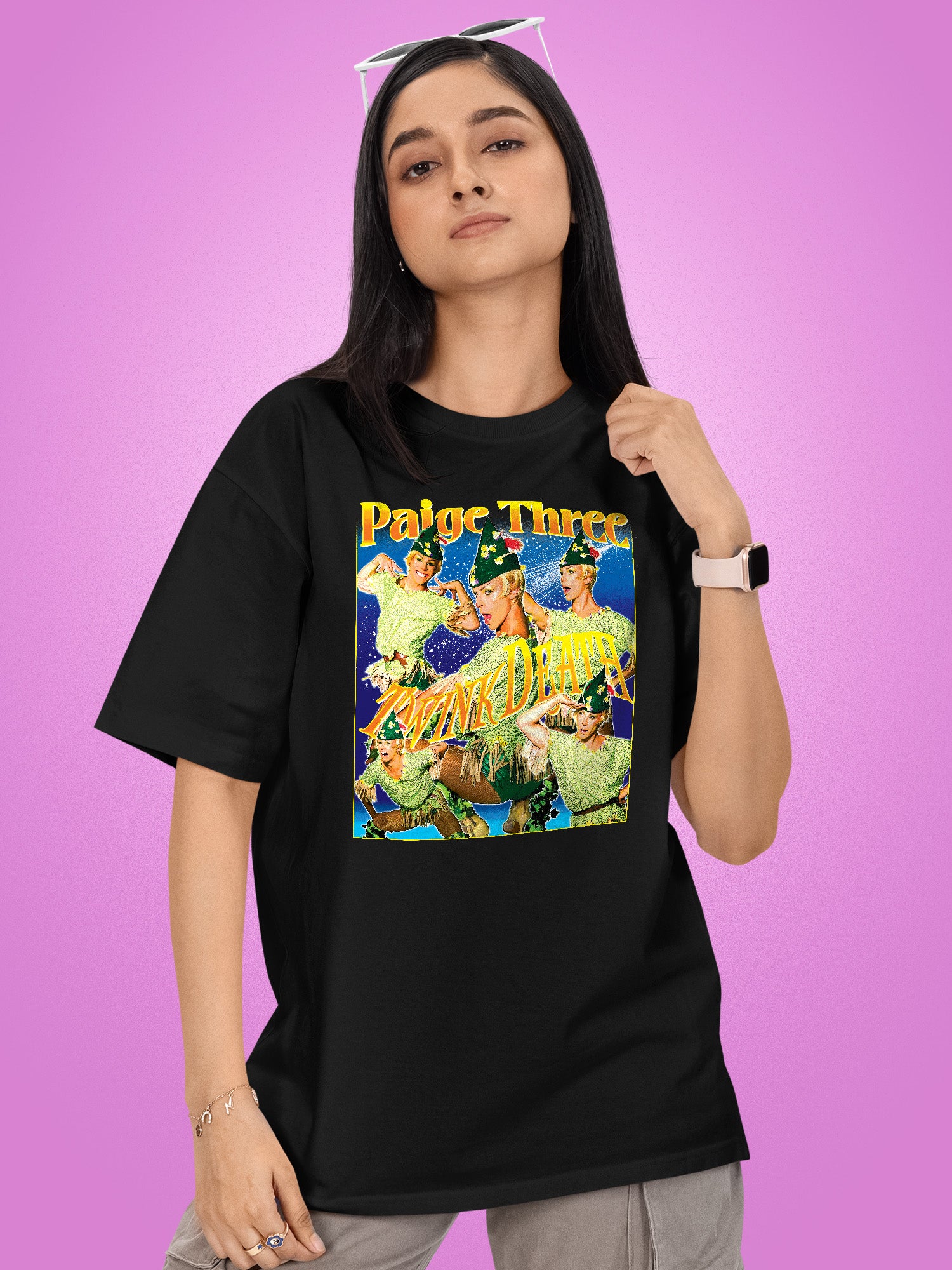 Person wearing a black t-shirt with a colorful graphic design on a purple background. Paige Three from BBC RuPaul's Drag Race UK Season 7